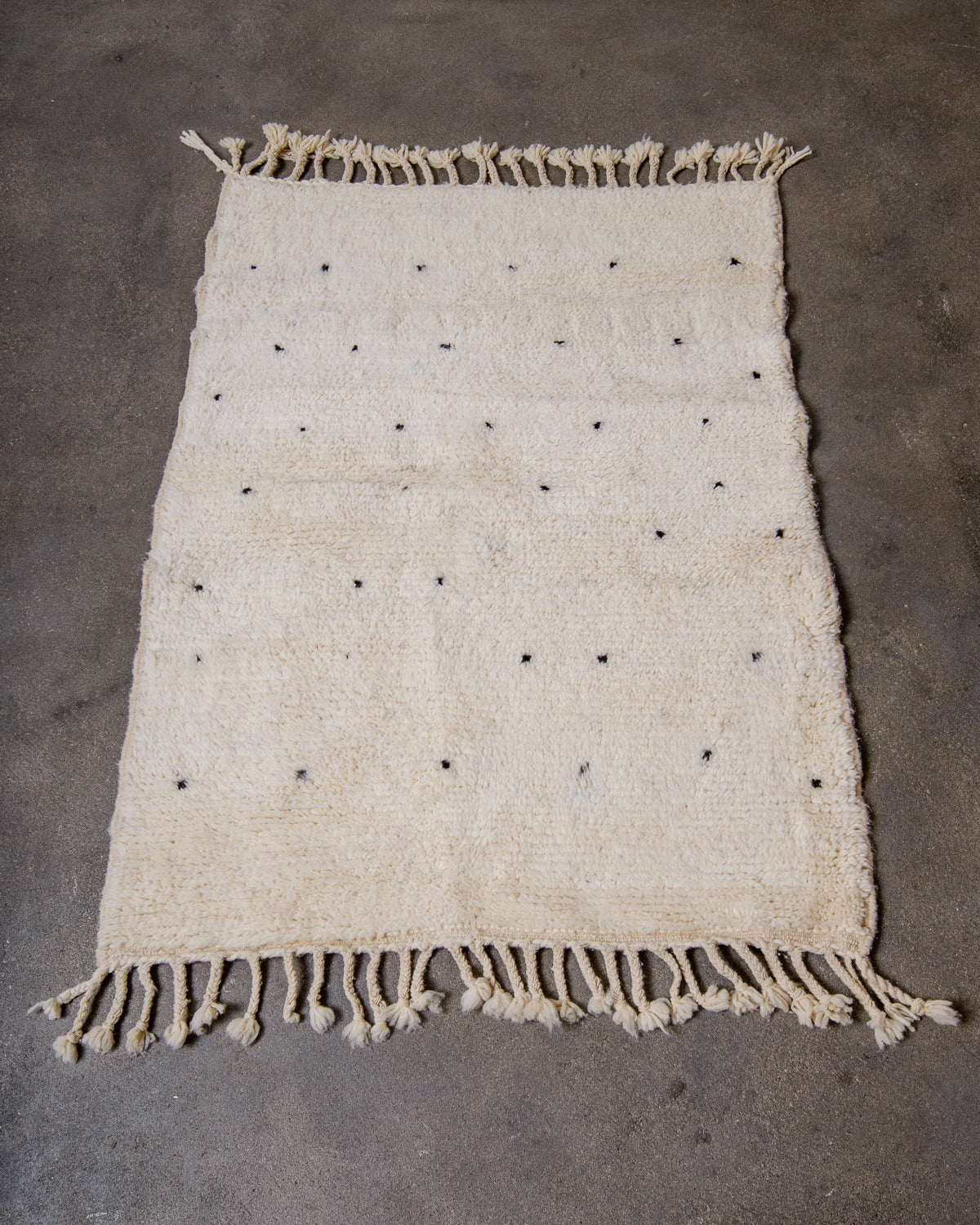 Beniourain rug in cream with black dots laying on concrete studio floor.
